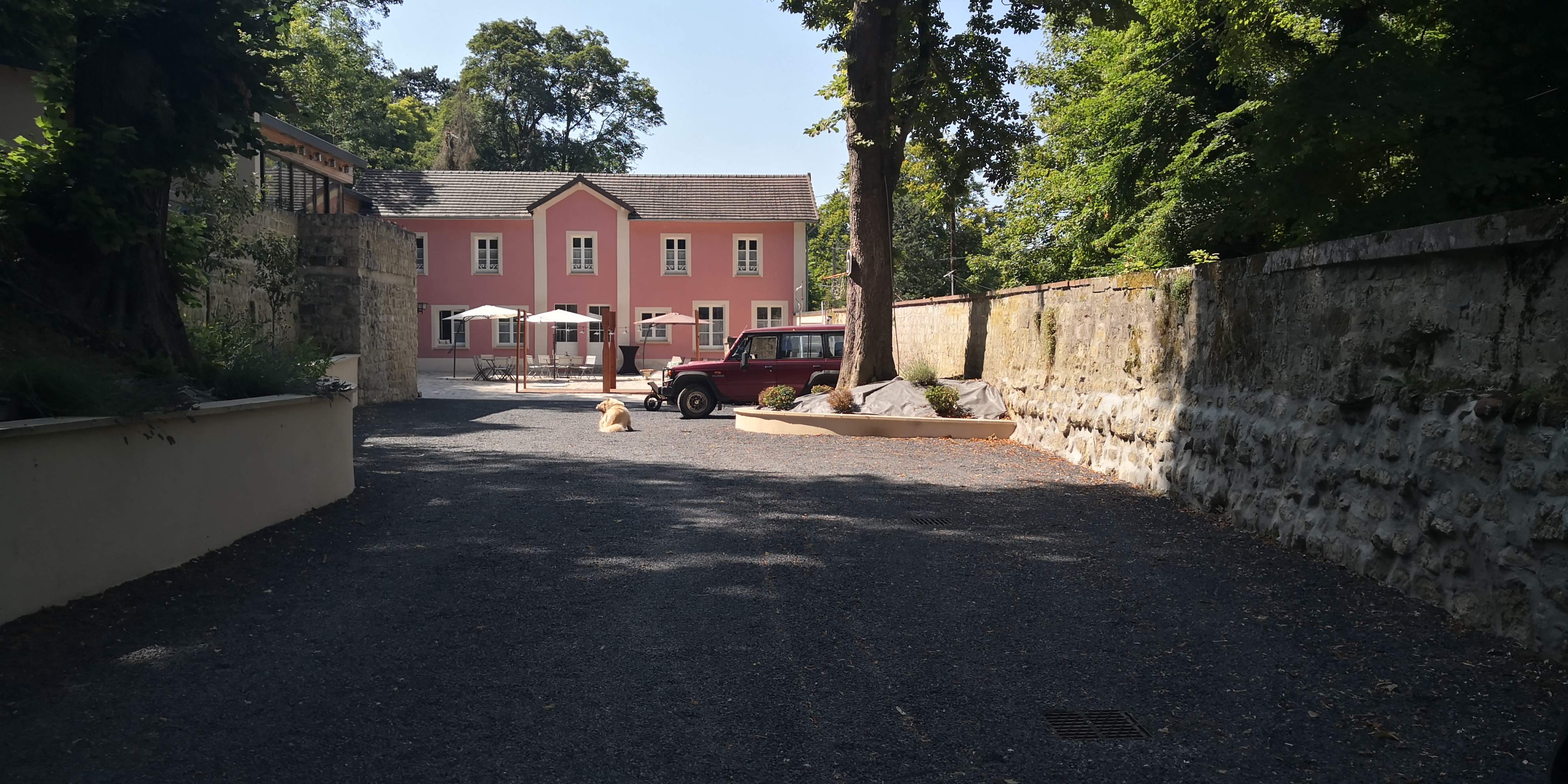 Allée gravillonnée entre deux murs en pierre menant à la façade rose de la maison d'hôtes.