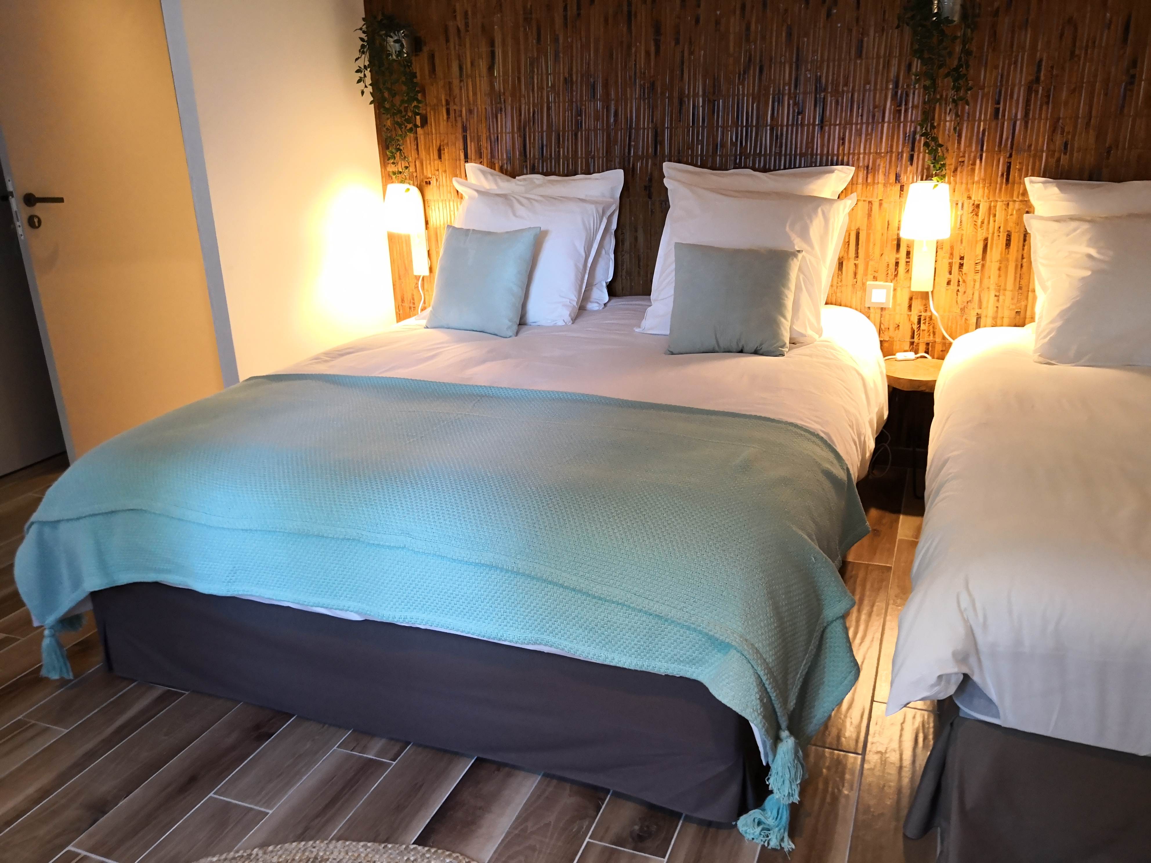 Lit avec tête de lit en bambou, coussins turquoise et jeté de lit assorti, dans une chambre au sol imitation parquet.
