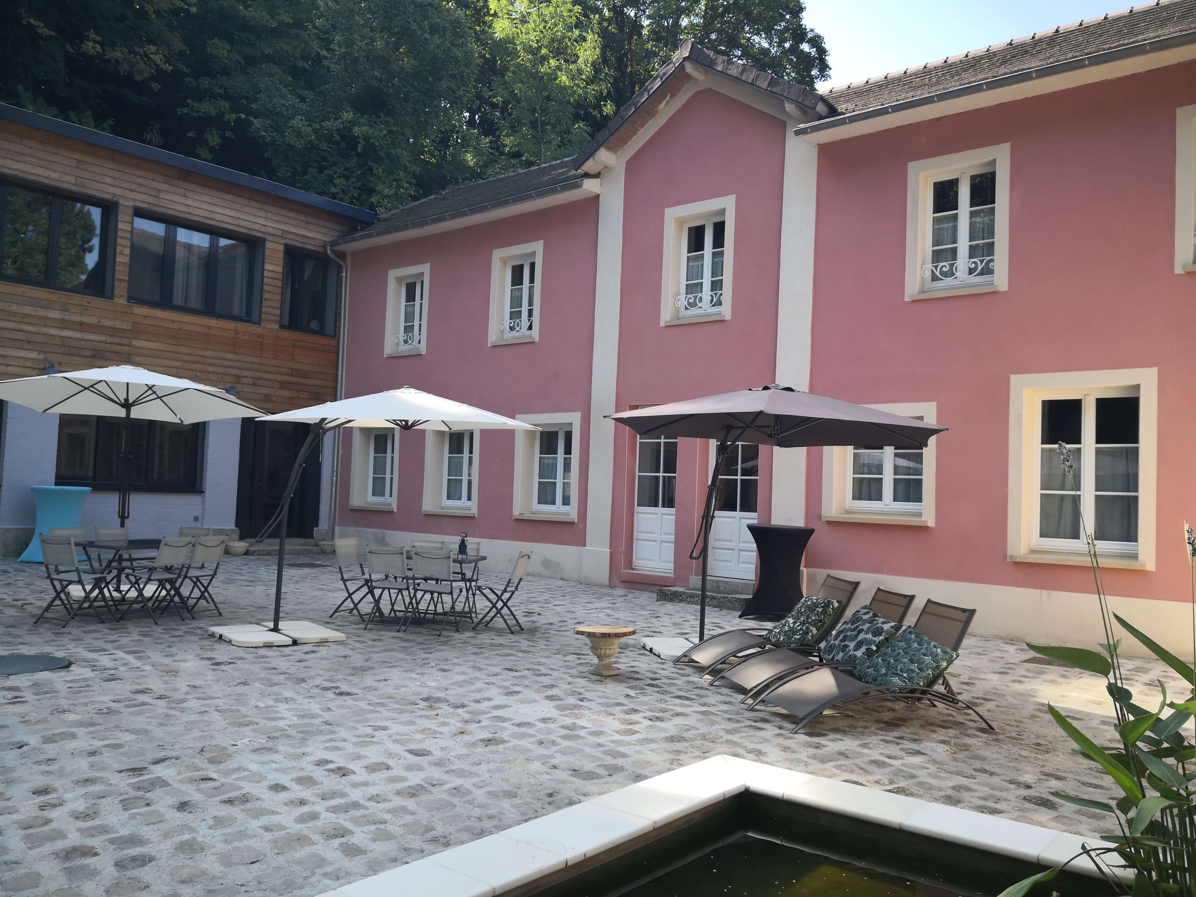 Façade rose de la maison d'hôtes et sa cour pavée, entourée d'arbres.