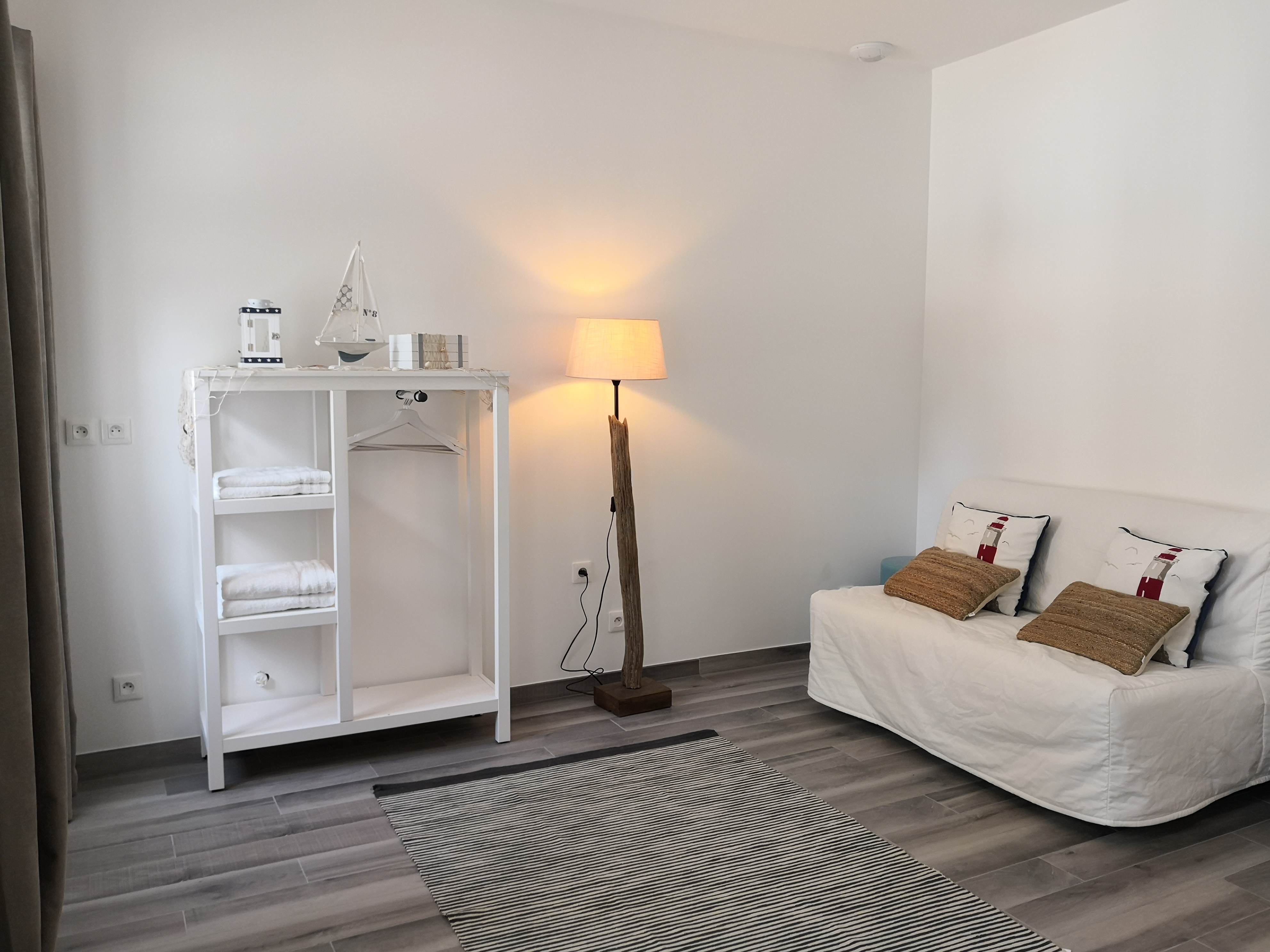 Coin penderie et banquette d'une chambre à thème marin, avec maquette de voilier, lampadaire en bois flotté et coussins à motif de phare.
